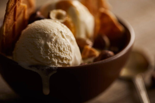 selective focus of of delicious melting ice cream in bowl with pieces of waffle 