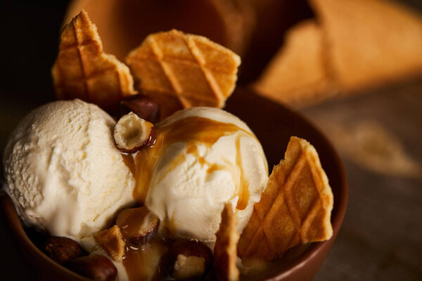 close up of delicious ice cream with pieces of waffle, caramel and hazelnuts in bowl 