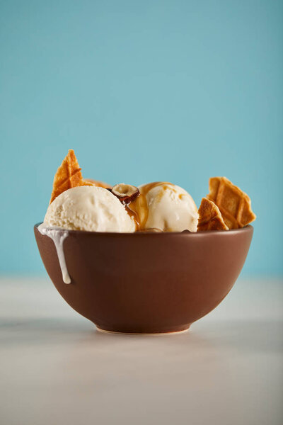 bowl of delicious ice cream with pieces of waffle and carmel on blue 