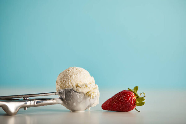 scoop of delicious ice cream in spoon and strawberry on blue with copy space