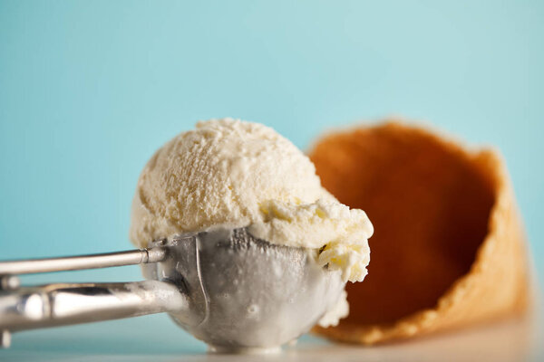 selective focus of ice cream scoop in spoon and waffle cone on blue 