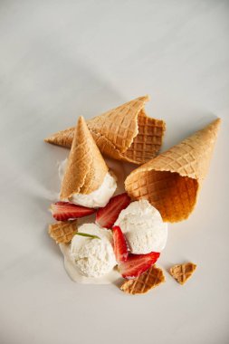 top view of waffle cones and delicious melting ice cream with strawberries on grey clipart