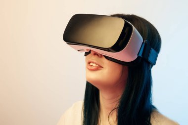 cheerful brunette girl wearing virtual reality headset on beige and blue clipart