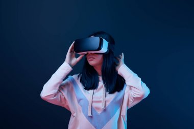 young brunette woman touching virtual reality headset on blue  clipart