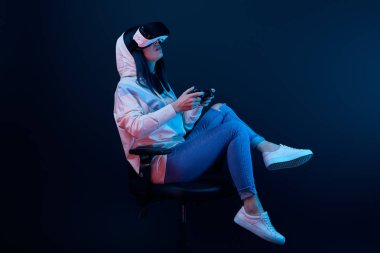 Kiev, Ukrayna - 5 Nisan 2019: Esmer kadın ekranda otururken ve mavi sanal gerçeklik kulaklık giyerken video oyunu oynarken 