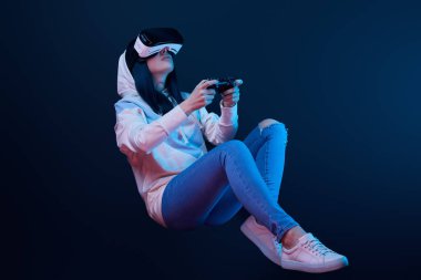 Kiev, Ukrayna - 5 Nisan 2019: Mavi sanal gerçeklik kulaklık video oyunu oynarken joystick tutan genç kadın düşük açı görünümü  