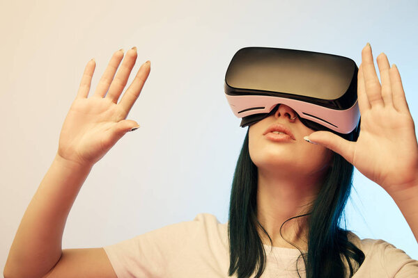 brunette girl wearing virtual reality headset and gesturing on beige and blue