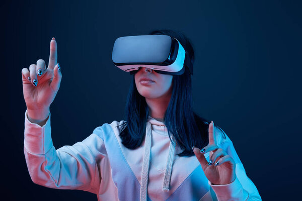 selective focus of young woman wearing virtual reality headset and pointing with fingers on blue 