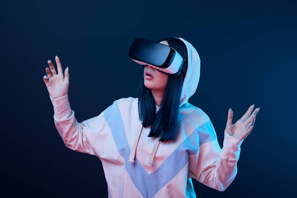 surprised brunette woman gesturing while using virtual reality headset on blue 