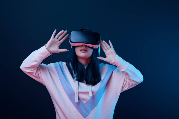 surprised young woman gesturing while using virtual reality headset on blue 