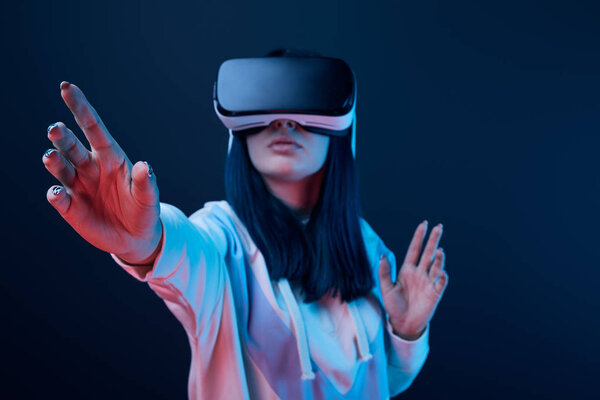 selective focus of young woman gesturing while using virtual reality headset on blue 