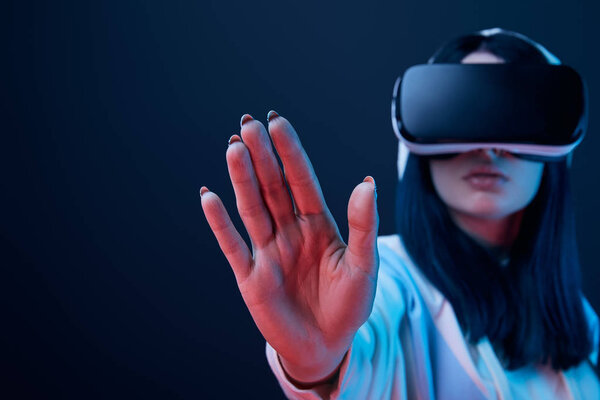 selective focus of hand of girl using virtual reality headset and gesturing on blue 