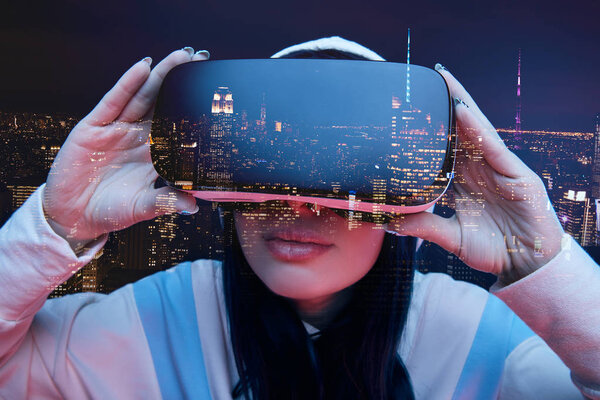 double exposure of brunette girl touching virtual reality headset and modern city with skyscrapers in nighttime 