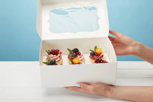 青で隔離されたカップケーキを持つ箱を持つ女性の部分的なビュー — ストック写真