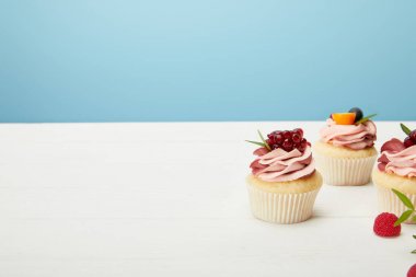 mavi izole beyaz yüzeyüzerinde çilek ve krem ile cupcakes