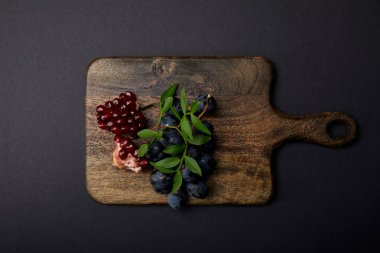 siyah yüzeyüzerinde ahşap kesme tahtası üzerinde üzüm ve garnet üst görünümü