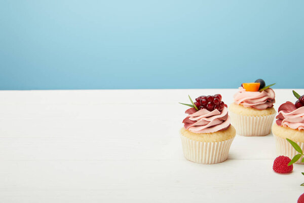 cupcakes with berries and cream on white surface isolated on blue