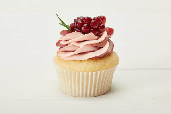 tasty cupcake with cream and garnet on white surface