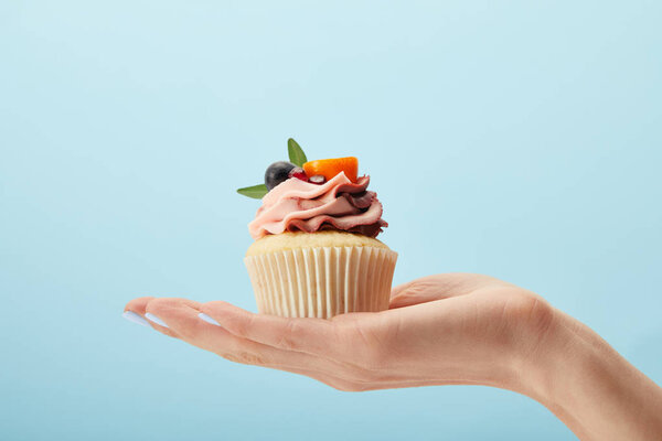 partial view of woman holding cupcake with cream isolated on blue