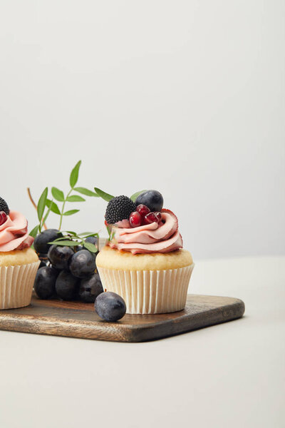 wooden cutting board with sweet cupcakes isolated on grey
