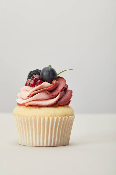cupcake with cream, garnet, grape and blackberry isolated on grey