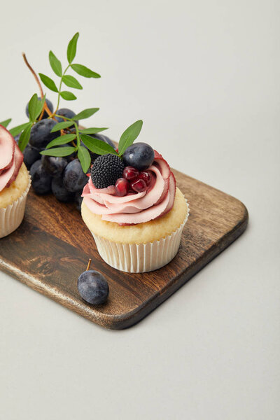 cupcakes with grapes on cutting board isolated on grey