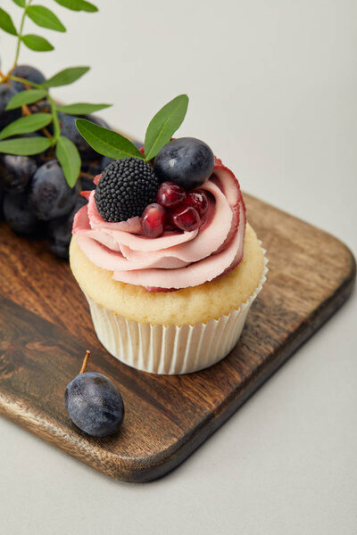 cupcake with cream and grapes on cutting board isolated on grey
