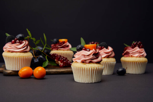 sweet cupcakes with berries and fruits on grey surface isolated on black