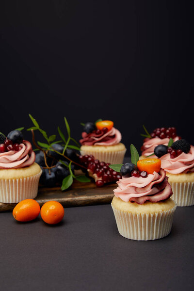 cupcakes with cream, fruits and berries on grey surface isolated on black