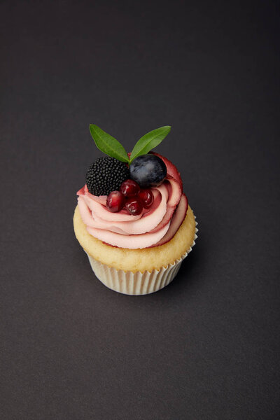 кекс со сливками, гранатом, виноградом и ежевикой на черной поверхности
