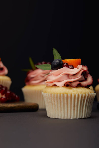 cupcakes with fruits and berries on grey surface isolated on black