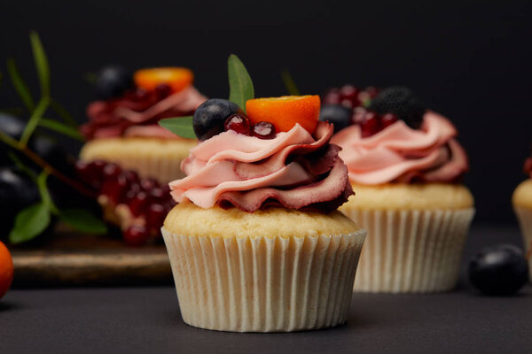 cupcakes with fruits and berries on grey surface isolated on black