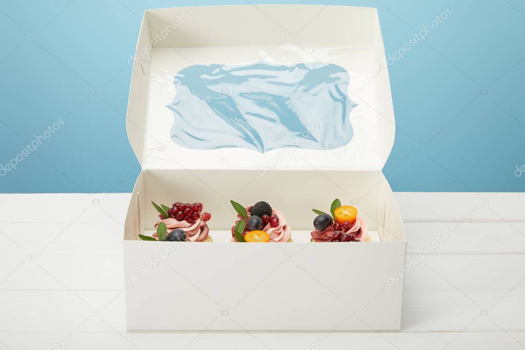 box with cupcakes on white surface isolated on blue