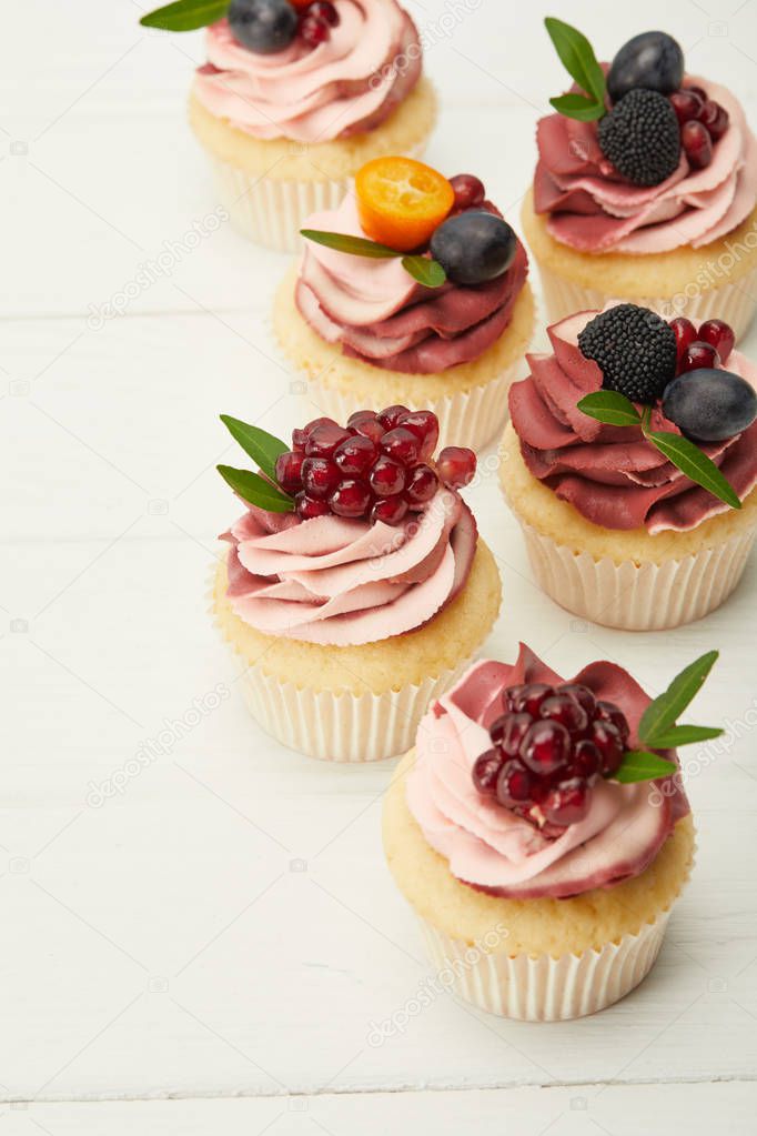 selective focus of cupcakes with cream and berries on white surface