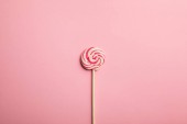 top view of delicious multicolored swirl lollipop on wooden stick on pink background
