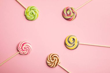 top view of delicious multicolored swirl lollipops on wooden sticks on pink background clipart