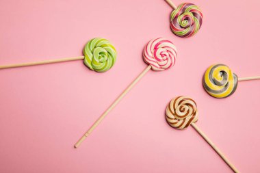 top view of delicious colorful swirl lollipops on wooden sticks on pink background clipart