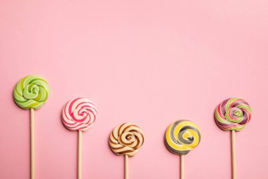 top view of delicious multicolored lollipops on wooden sticks on pink background clipart