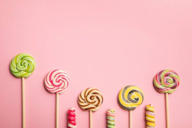 top view of delicious swirl lollipops on wooden sticks on pink background with copy space clipart