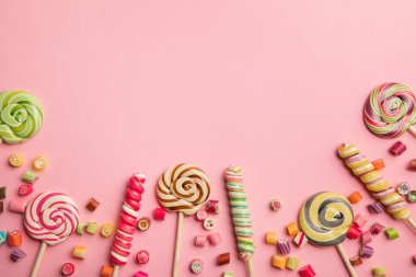 pembe arka plan üzerinde ahşap çubuklar ve şekerler üzerinde lezzetli çok renkli girdap lolipop üst görünümü