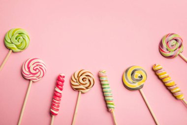 top view of multicolored swirl lollipops on wooden sticks on pink background clipart