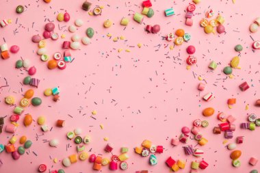 top view of multicolored candies and sprinkles scattered on pink background  clipart