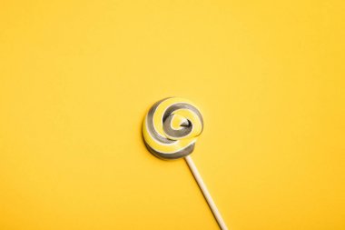 top view of delicious multicolored swirl lollipop on wooden stick on yellow background clipart