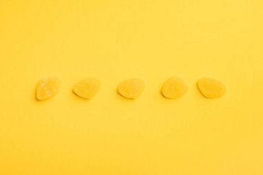 top view of delicious sugary jellies in row on yellow background clipart