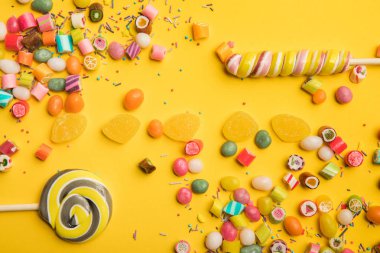 sarı arka plan üzerinde lezzetli çok renkli şekerler, jöleler, serpintiler ve lolipop üst görünümü