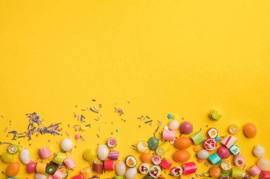çok renkli lezzetli şekerler üst görünümü ve kopya alanı ile sarı arka plan üzerinde dağınık sprinkles