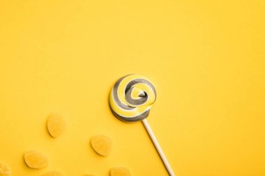 top view of delicious round lollipop on wooden stick and jellies on yellow background clipart