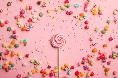 dağınık karamel şekerler ile ahşap sopa üzerinde lezzetli girdap lolipop üst görünümü ve pembe arka plan üzerinde serpin