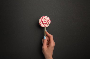 cropped view of woman holding round tasty lollipop on black background clipart