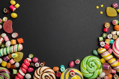top view of delicious multicolored swirl and round lollipops, candies, jellies and sprinkles on black background clipart